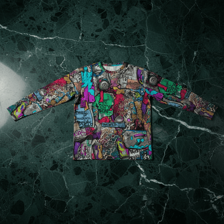 Aerosol Alchemists long sleeve tee by Dyles Mavis — dense graffiti sticker-bomb all-over print with spray cans, tags and street art panels in magenta, teal and green, front flat lay on marble