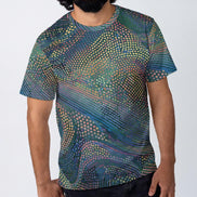 Halftone Drift t-shirt by Dyles Mavis — all-over print of halftone dot-matrix waves in teal, purple and gold flowing in diagonal bands, worn by a man against a plain background
