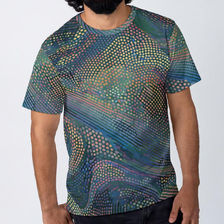 Halftone Drift t-shirt by Dyles Mavis — all-over print of halftone dot-matrix waves in teal, purple and gold flowing in diagonal bands, worn by a man against a plain background