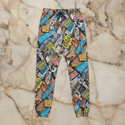 Tag Stack Riot lounge pants by Dyles Mavis — heavyweight cotton sweatpants with all-over print of a dense street-sticker and graffiti tag collage in blue, pink, yellow and black, flat lay on marble