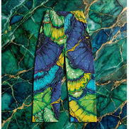 Butterfly Wing pajama pants by Dyles Mavis — brushed polyester lounge pants with all-over print of emerald and sapphire organic butterfly wing scale patterns and gold vein detailing, flat lay on green marble