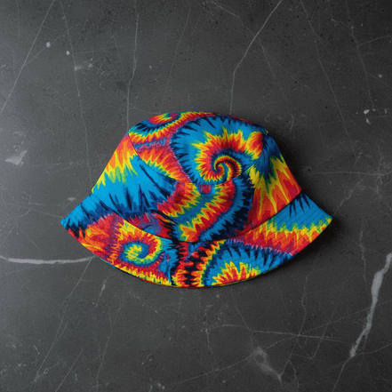 Tie-Dye Spiral Reversible Bucket Hat with classic rainbow tie-dye spirals in red, blue, yellow, and orange at full saturation, flat lay on dark marble