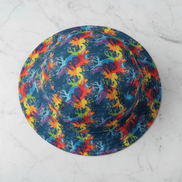 Neon Anemone Bucket Hat from above with electric coral and anemone splash pattern in rainbow red, yellow, blue, and purple on deep navy ground, on white marble