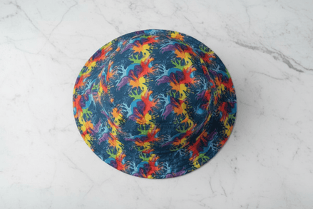 Neon Anemone Bucket Hat from above with electric coral and anemone splash pattern in rainbow red, yellow, blue, and purple on deep navy ground, on white marble