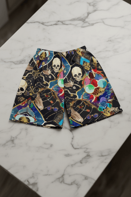 Dearly Departed Basketball Shorts in black performance fabric with skull, skeleton hand, and jewel mosaic collage in cream, teal, red, gold, and blue, flat lay on marble