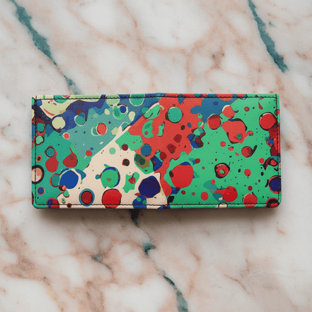 Paint Splat Confetti Leather Wallet handmade bifold in white leather with multicolor paint splat drip-dots in green, red, blue, and cream, flat lay on pink marble