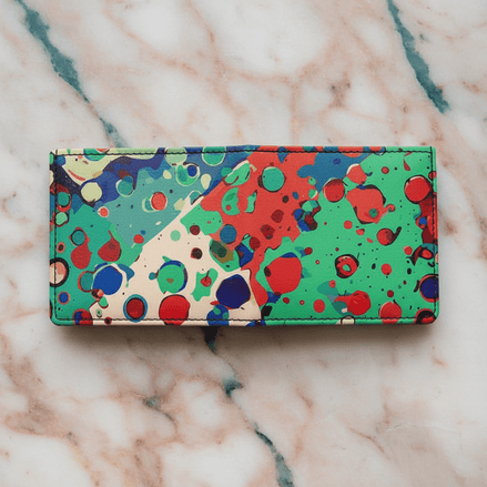 Paint Splat Confetti Leather Wallet handmade bifold in white leather with multicolor paint splat drip-dots in green, red, blue, and cream, flat lay on pink marble