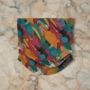 Painted Camo Neck Gaiter in quick-dry fabric with multicolor brush-dab pattern in orange, teal, crimson, magenta, and green, folded flat on marble