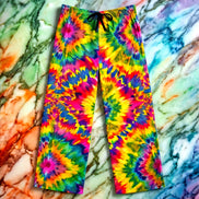 Rainbow Vortex Pajama Pants relaxed lounge cut with electric starburst tie-dye rosettes in pink, gold, green, blue, and violet, black drawstring, flat lay on rainbow marble
