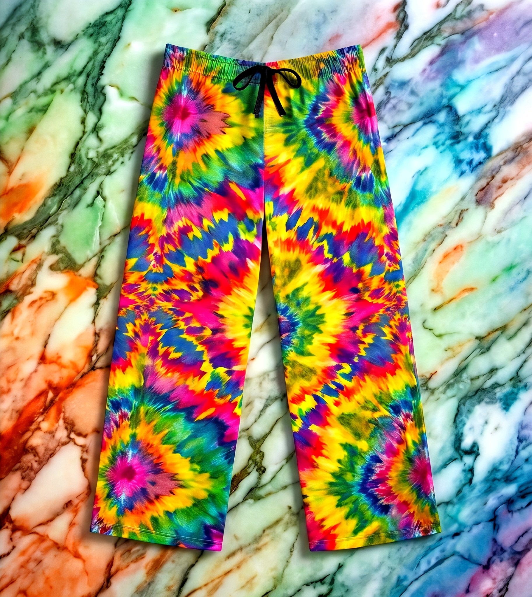 Rainbow Vortex Pajama Pants relaxed lounge cut with electric starburst tie-dye rosettes in pink, gold, green, blue, and violet, black drawstring, flat lay on rainbow marble